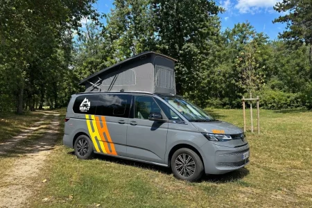 Van aménagé California T7 avec toit relevable stationné dans un environnement naturel.