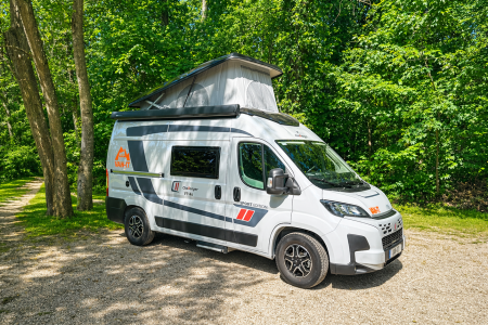 Le Matador de VAN-IT stationné en pleine nature, avec toit relevable ouvert, sur un chemin entouré d’arbres et de verdure.