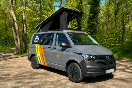 Venturo + de VAN-IT gris avec toit relevable ouvert, stationné sur un chemin en forêt dans un cadre naturel et ensoleillé.