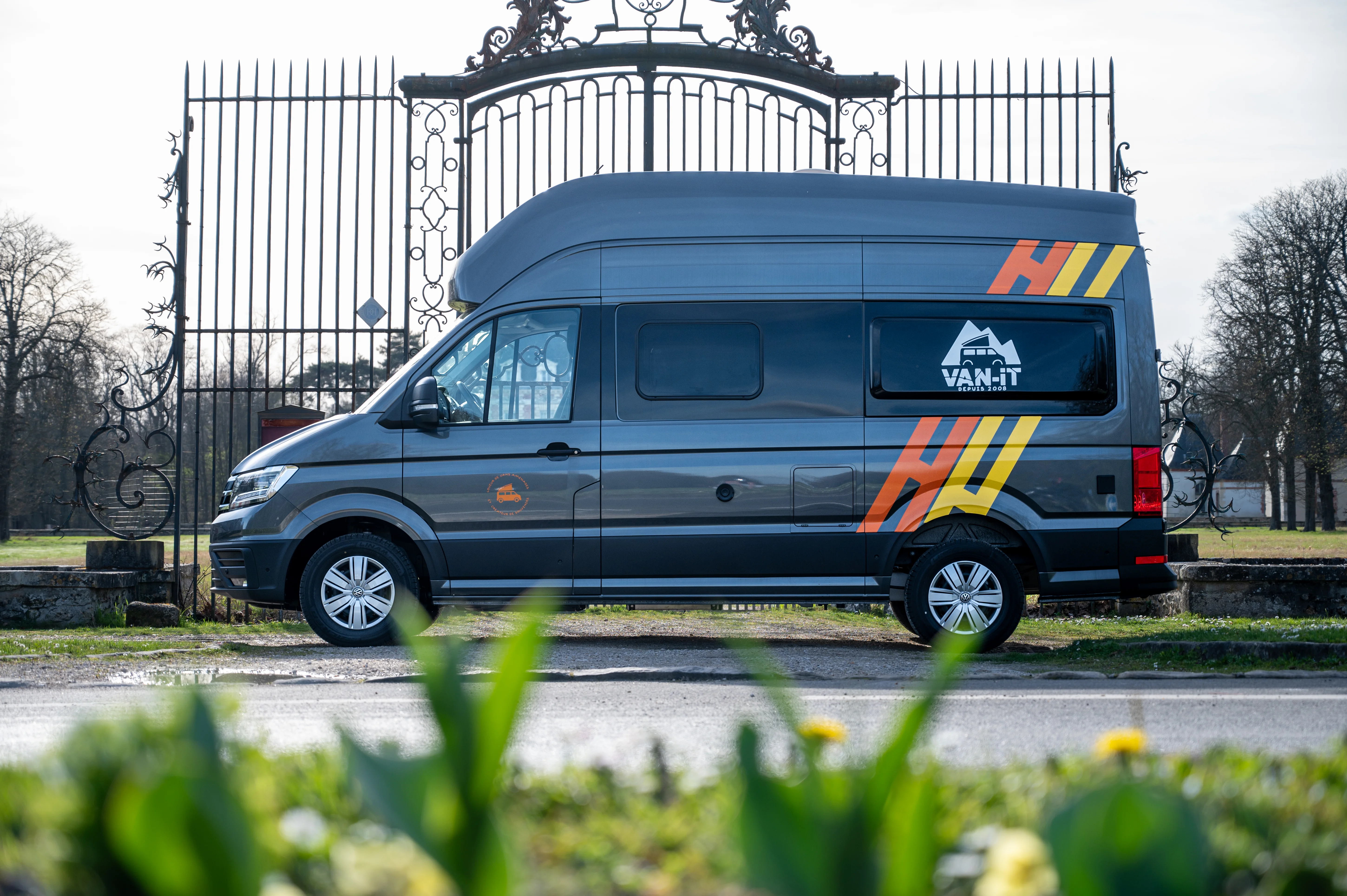 Volkswagen Grand California vue de profil stationné devant un portail.