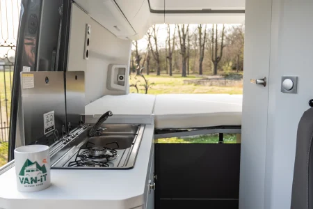 Intérieur du Volkswagen Grand California avec cuisine équipée, évier, plaque de cuisson et lit arrière.