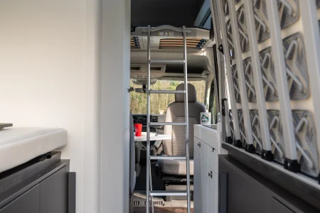 Intérieur du van Volkswagen Grand California avec échelle vers le lit supérieur et espace de vie.
