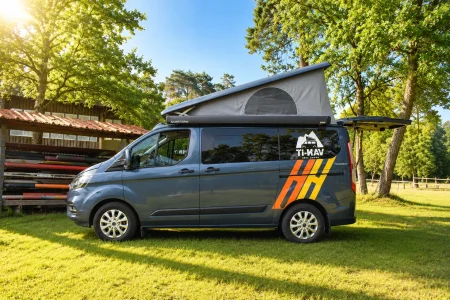 Ford Nugget VAN-IT avec toit relevable, stationné dans un environnement verdoyant et ensoleillé.