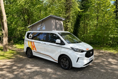 Van aménagé Ford Panama avec toit relevable stationné dans un environnement naturel.