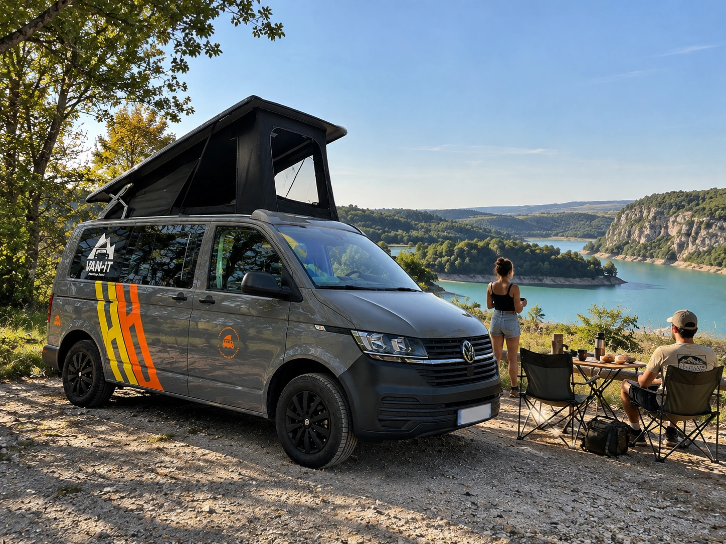 Van aménagé VAN-IT gris au bord du lac de Vouglans, dans un paysage de collines boisées.